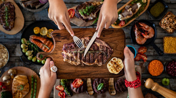 A person holds a cutting board while another slices meat over a Thanksgiving feast on the table.
