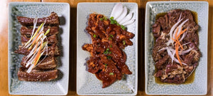 Three plates of grilled exotic meats with garnishes on rectangular dishes