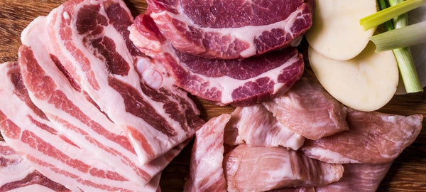 Assorted raw pork cuts including pork belly slices and ribs on a wooden board with vegetables