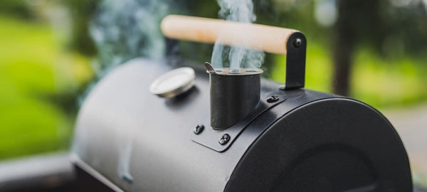 Smoke rising from a backyard charcoal grill with temperature gauge