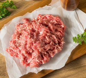 Fresh raw lean ground pork on parchment paper with herbs on a wooden board