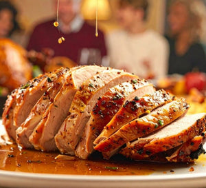 Sliced roasted turkey breast drizzled with juices on a serving platter at a dinner table