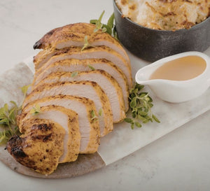 Sliced roasted turkey breast with gravy and herbs on a serving board